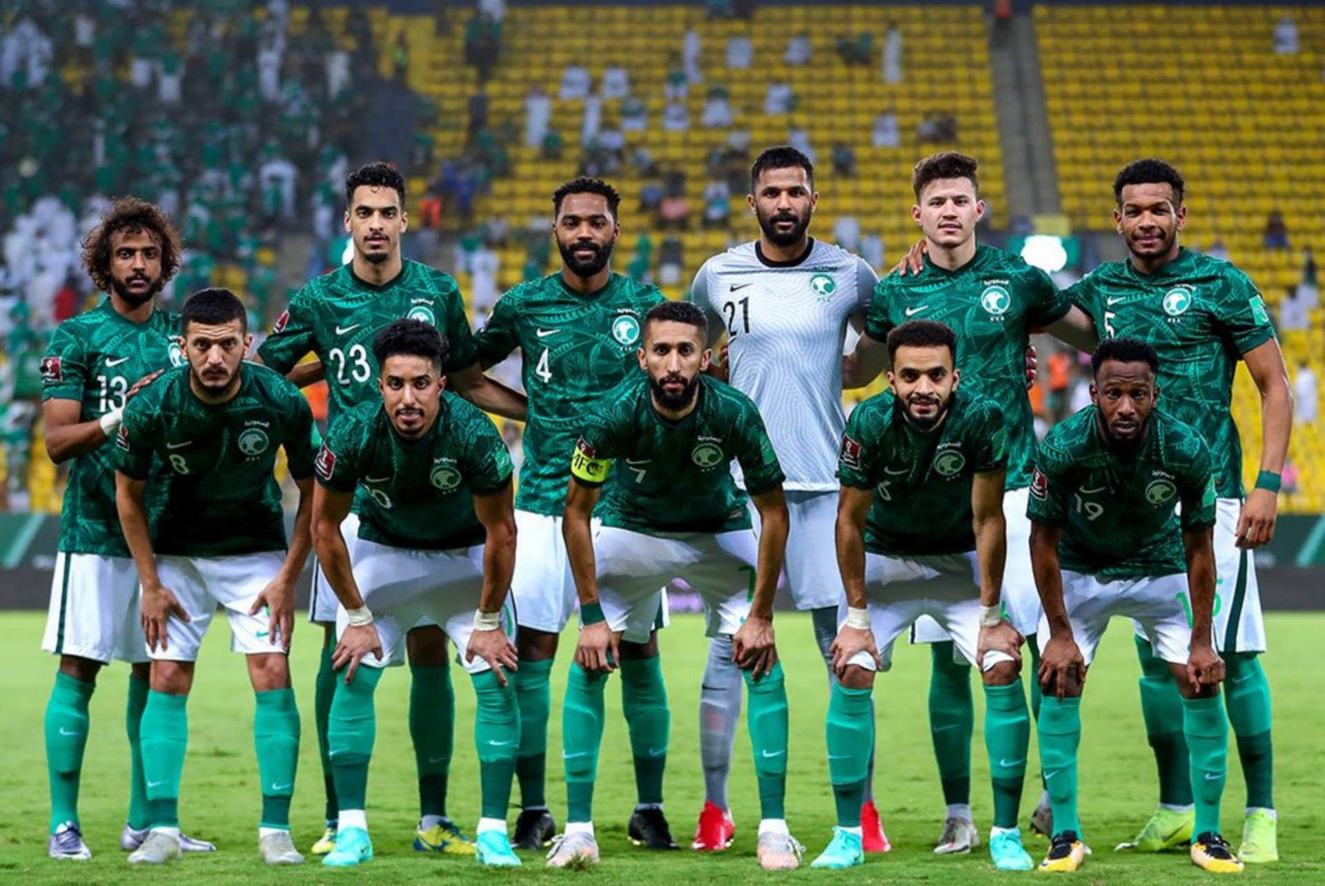 Football team in green uniforms posing for a group photo on the field with a stadium background.